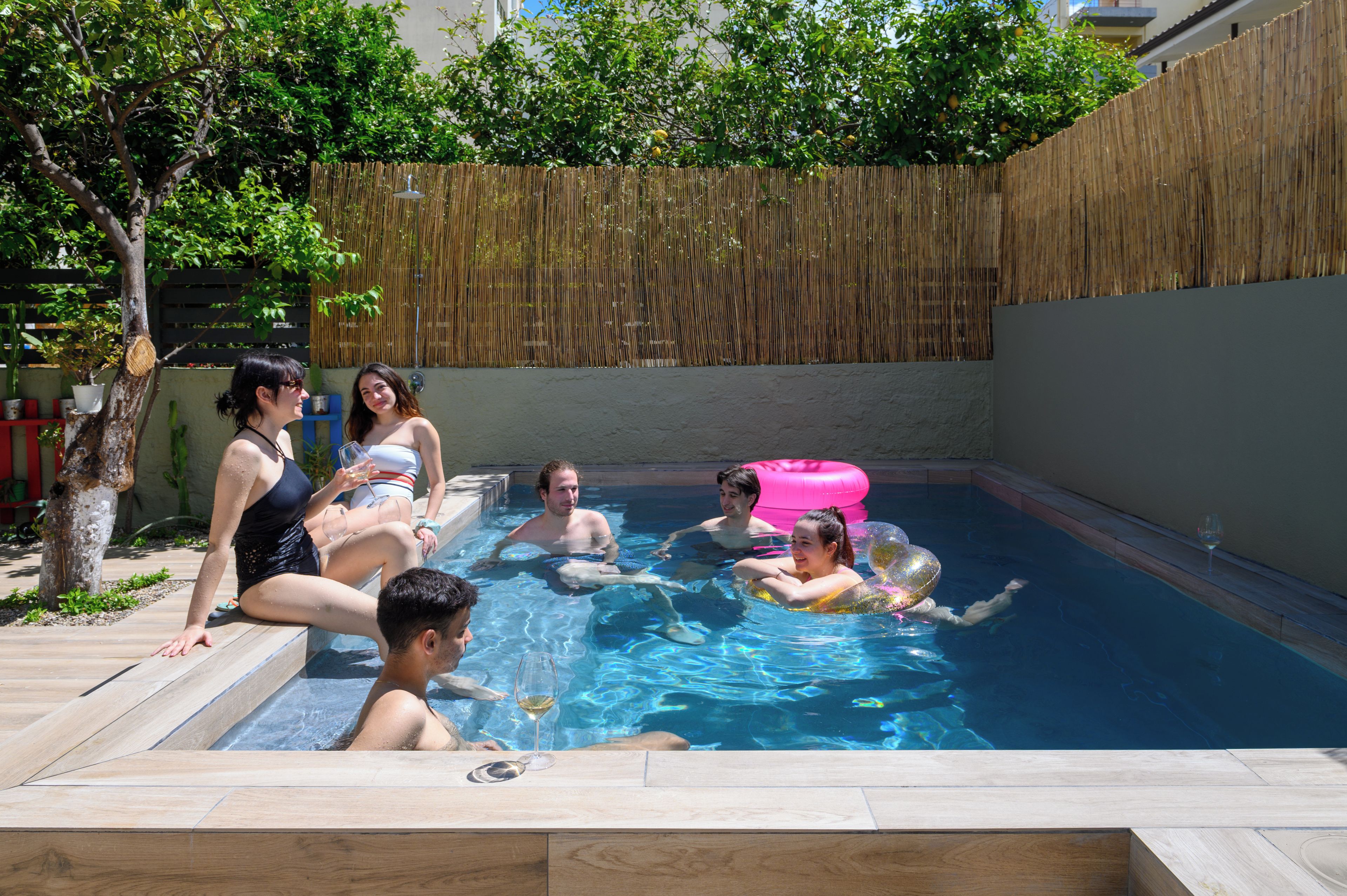 A swimming pool with people enjoying the water, surrounded by a wooden fence and trees.