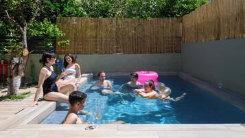 A swimming pool with people enjoying the water, surrounded by a wooden fence and trees.