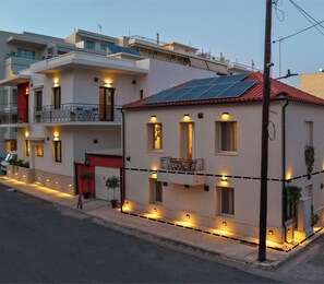A modern two-story building with solar panels on the roof, outdoor lighting along the ground floor, and a visible garage door.