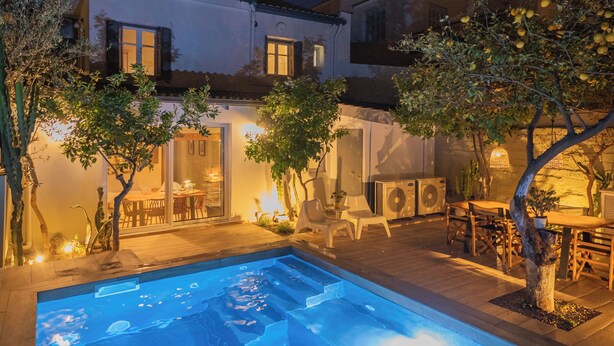 A swimming pool with a patio area, outdoor furniture, and a building with multiple windows and balconies.