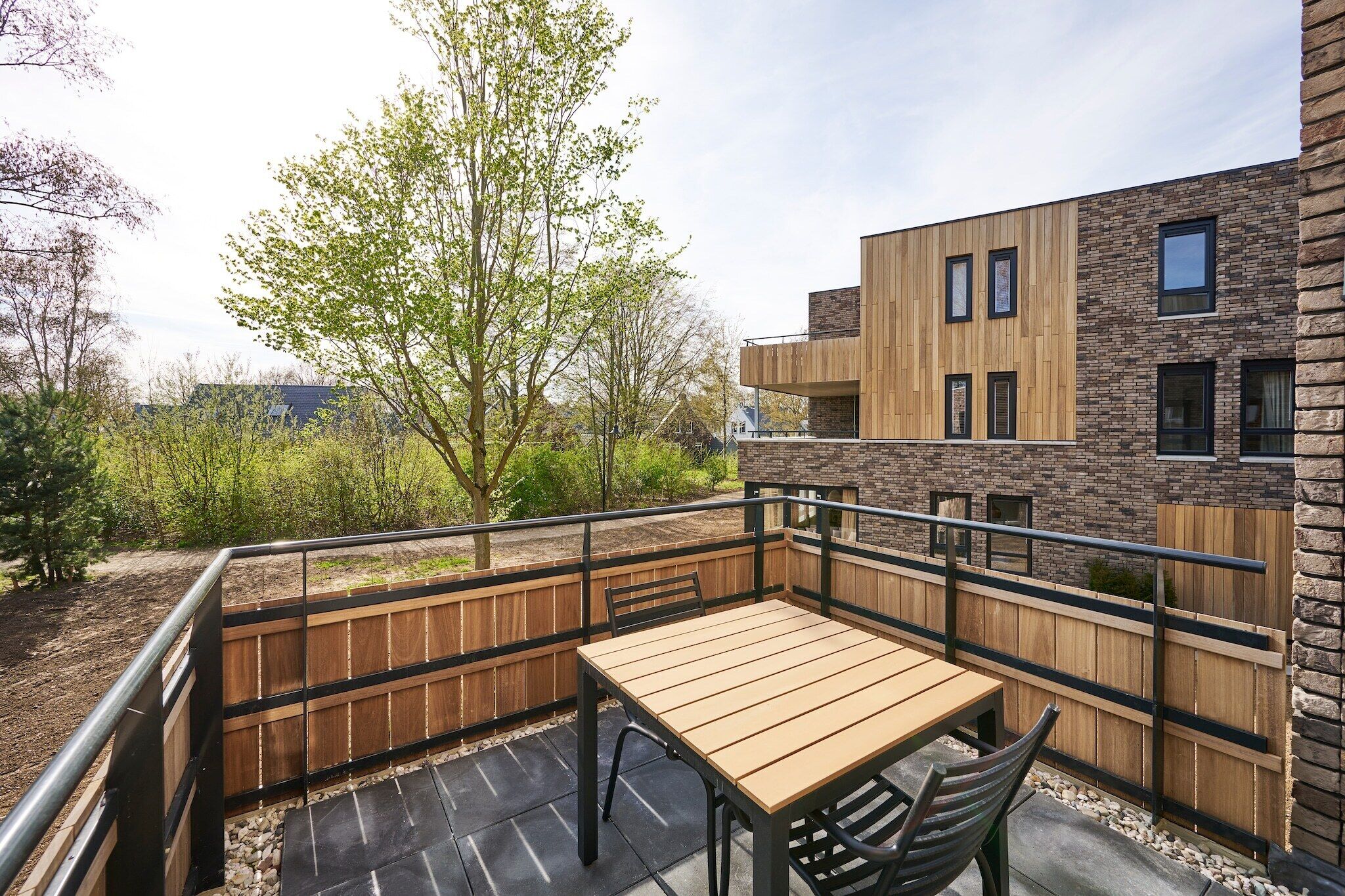 Un patio con una mesa y sillas de madera, rodeado por una cerca de madera y un muro de piedra.