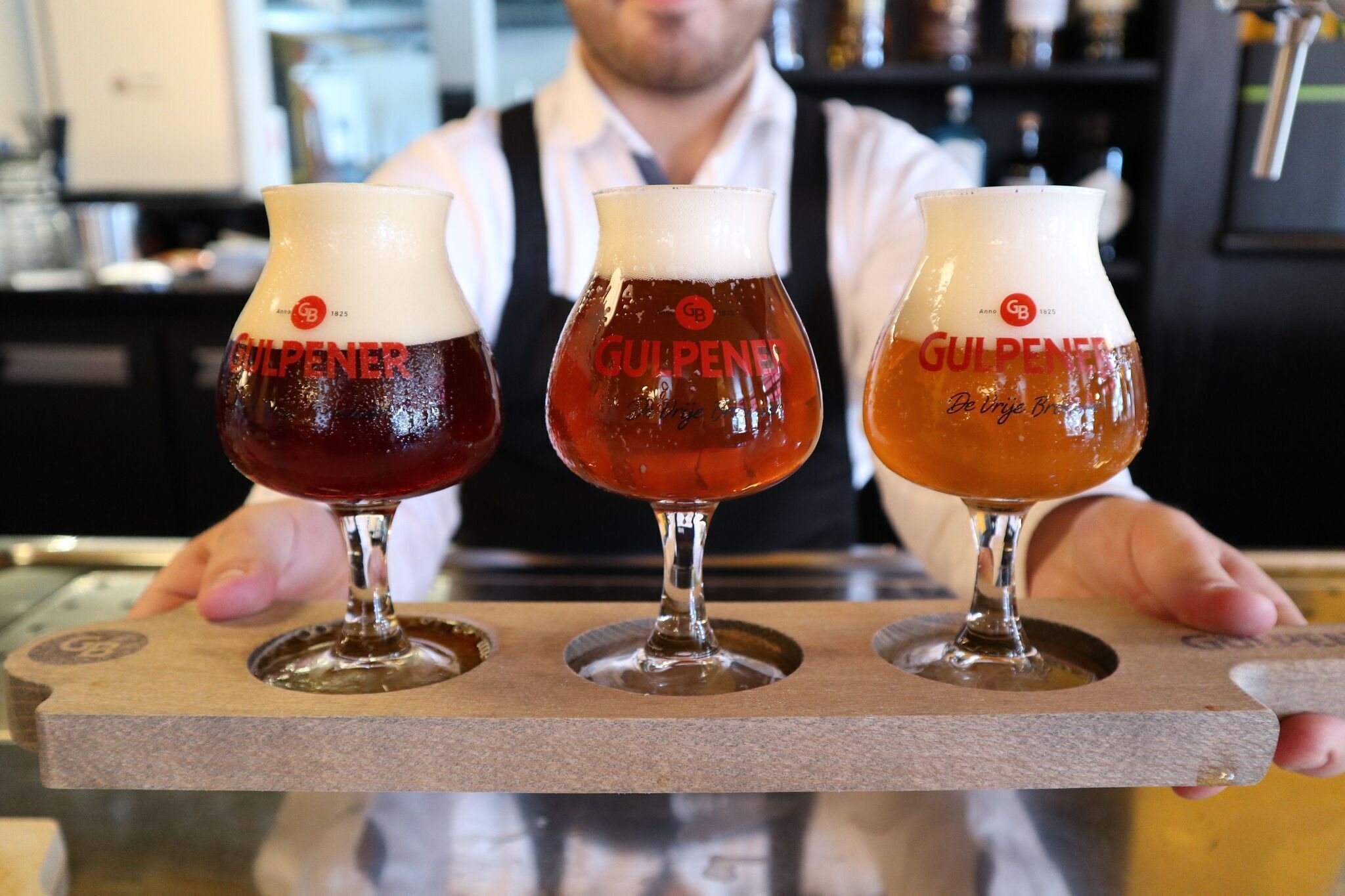 Three glasses of beer on a wooden tray.