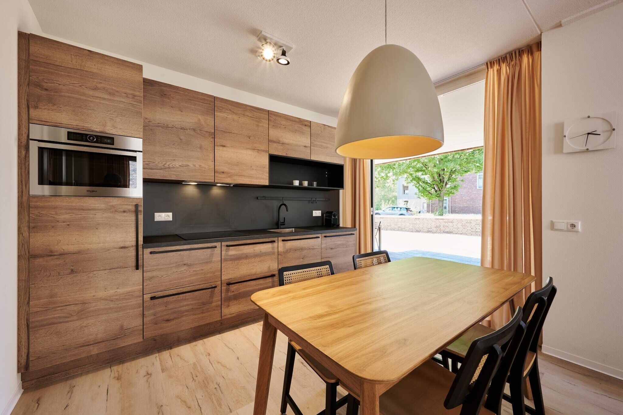 Une cuisine moderne avec des meubles en bois, un four encastré et un coin repas comprenant une table et des chaises en bois.