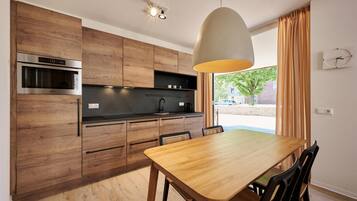 Une cuisine moderne avec des meubles en bois, un four encastré et un coin repas comprenant une table et des chaises en bois.