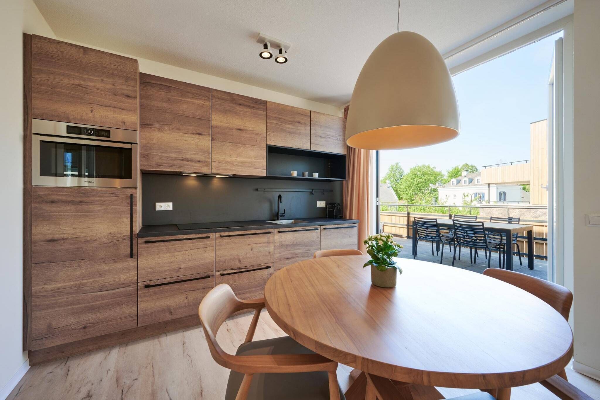 Une cuisine moderne avec des meubles en bois, un four encastré et un coin repas comprenant une table ronde et des chaises.