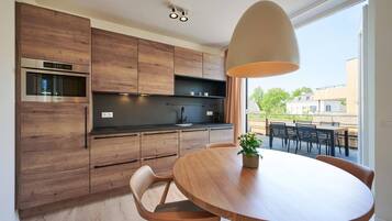 Une cuisine moderne avec des meubles en bois, un four encastré et un coin repas comprenant une table ronde et des chaises.