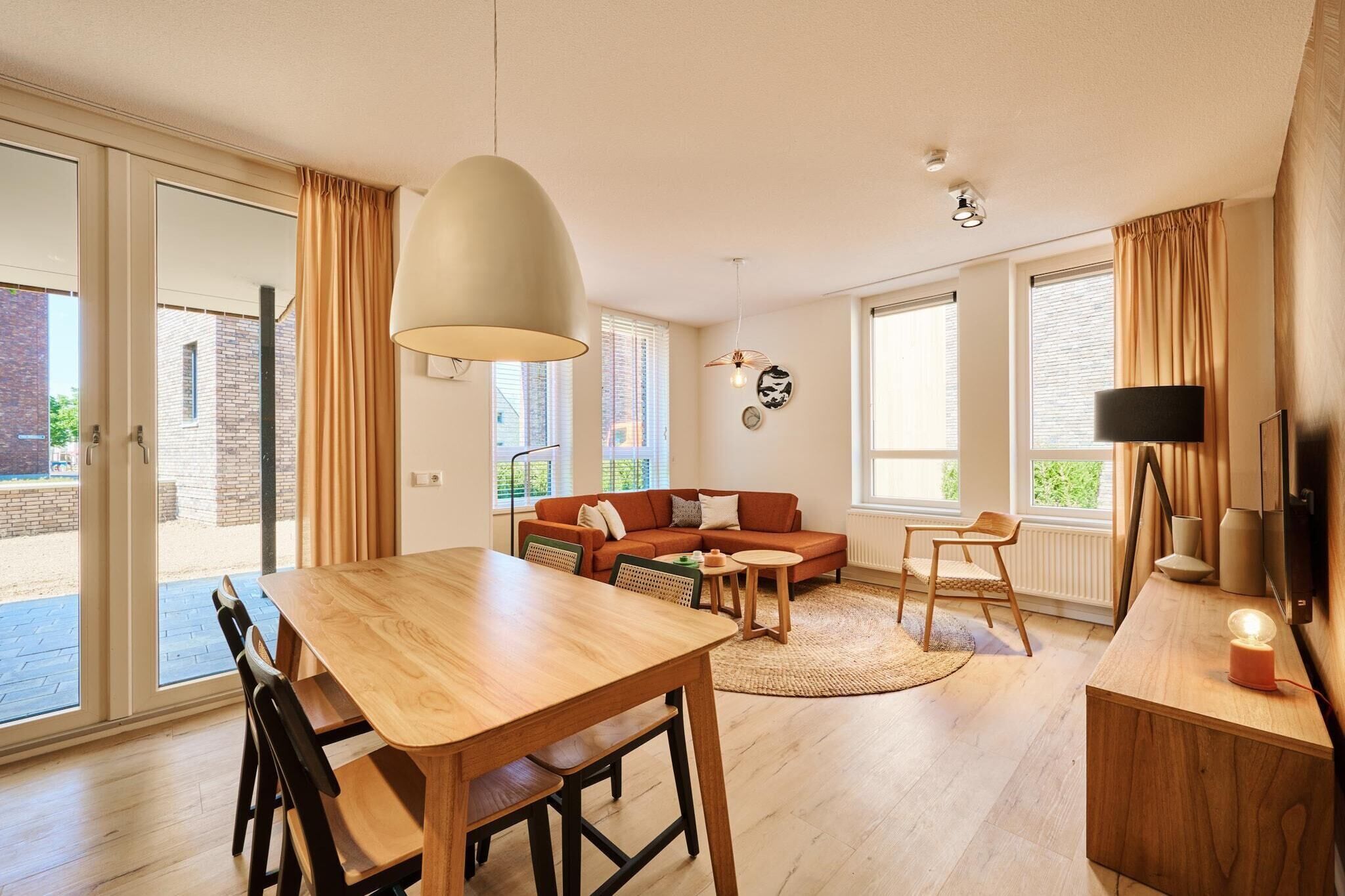 Een moderne woonkamer met een houten eettafel, een bank en een grote hanglamp.