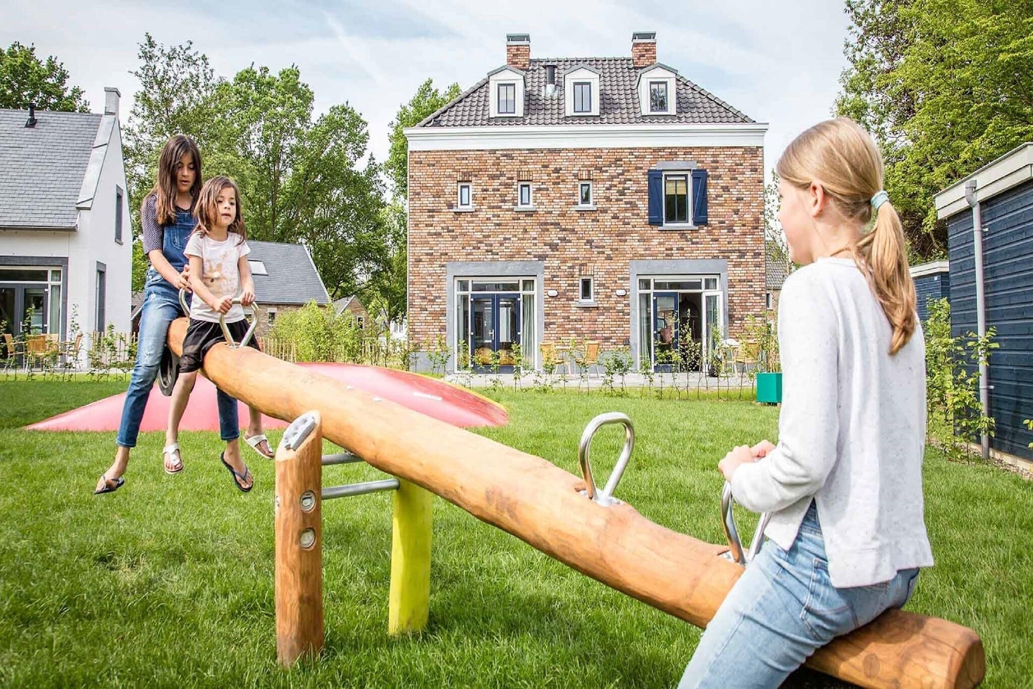 A playground with a seesaw and a brick house in the background.