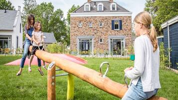 A playground with a seesaw and a brick house in the background.