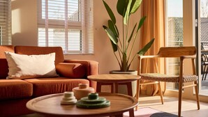Sala de estar com sofá, mesa de madeira redonda, planta em vaso e uma cadeira.
