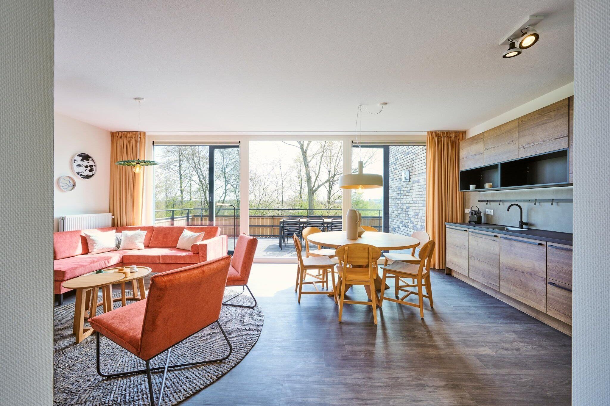 A modern living room with a sofa, chairs, a dining table, and a kitchen area with cabinets and a sink.