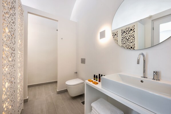 A modern bathroom with a white sink, mirror, and toilet. - Palm Island (Santorini)