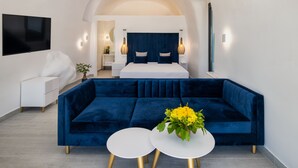 Un dormitorio moderno con una cama grande, un sofá azul, dos mesas redondas blancas y un televisor montado en la pared.
