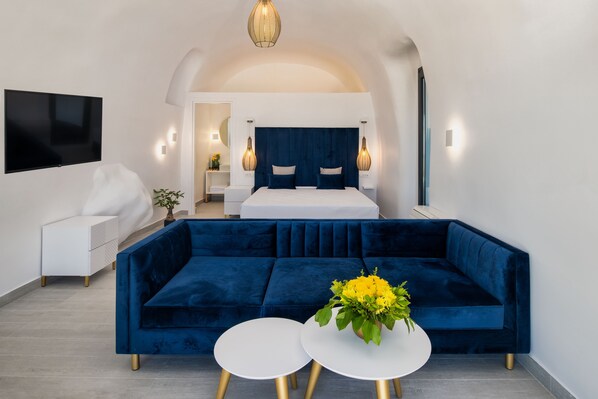 Un dormitorio moderno con una cama grande, un sofá azul, dos mesas redondas blancas y un televisor montado en la pared.
