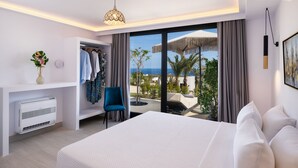 Habitación de hotel moderna con una cama grande, zona de estar con una silla azul, armario y vista al mar.