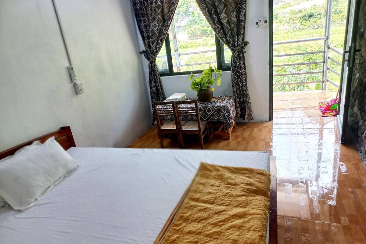 Een slaapkamer met een bed, een tafel met een plant en uitzicht op een groen landschap door een raam.