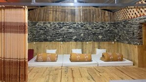 Quarto com parede de pedra, piso de madeira e três camas com almofadas florais.