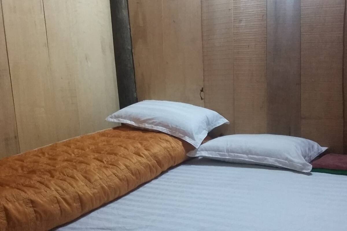 Een eenpersoonsbed met een bruin sprei en twee kussens, één wit en één roze, in een kamer met houten wanden.