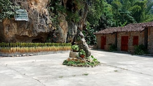 Um pátio com uma escultura de pedra, um edifício de pedra com portas vermelhas e uma placa numa parede rochosa.