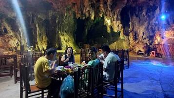 Un grupo de personas cenando en un restaurante cueva con mesas y sillas dispuestas en el espacio abierto.