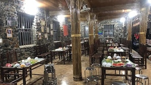 Restaurante com paredes de pedra, mobiliário de madeira e mesas preparadas para refeições.