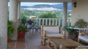 A balcony with wicker furniture, potted plants, and a view of a city and mountains.