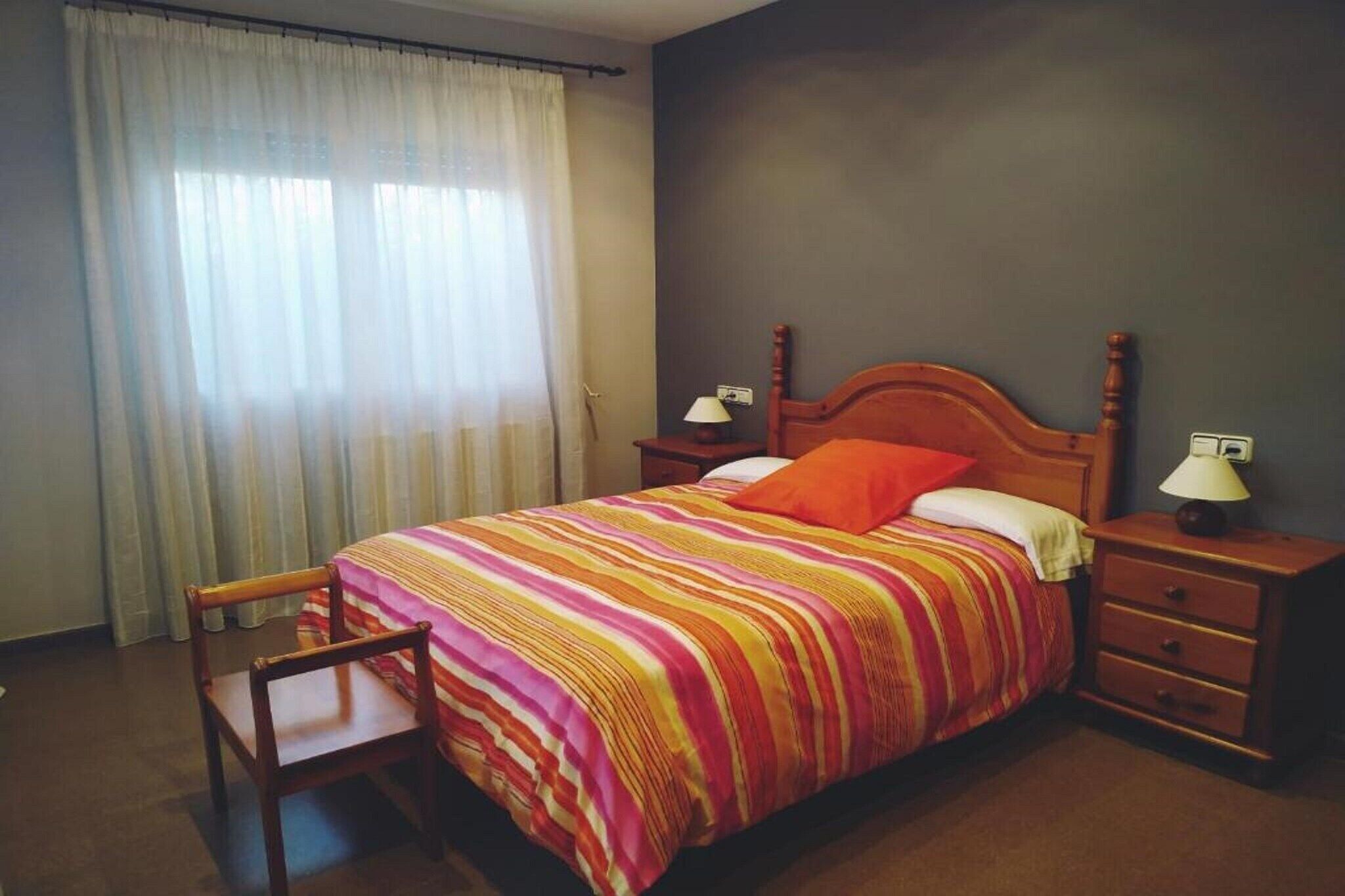 A hotel room with a bed, a chair, a nightstand, and a lamp.