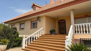 A two-story house with a tiled roof, a front porch with steps, and a large window.