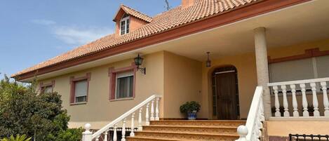 A two-story house with a tiled roof, a front porch with steps, and a large window.