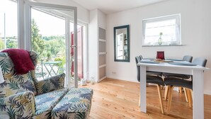 A modern living room with a sofa, dining table, and chairs. There is a large window with a view of greenery outside. - Pretty Holiday Home in Schleiden with Balcony and Barbecue (Schleiden)