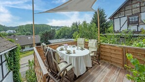 A wooden deck with a round table set for dining, surrounded by chairs, and a large canopy overhead. - Pretty Holiday Home in Schleiden with Balcony and Barbecue (Schleiden)