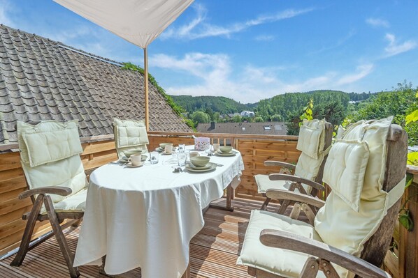 An outdoor dining area with a round table set for four, surrounded by wooden chairs with cushioned seats.