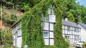 A traditional half-timbered house with ivy-covered walls, a visible chimney, and a parked car in front. - Pretty Holiday Home in Schleiden with Balcony and Barbecue (Schleiden)