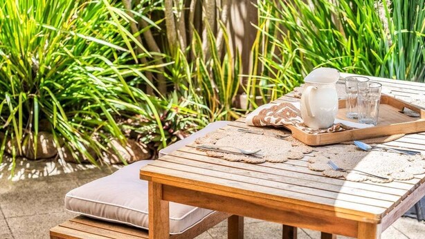 A wooden table set outdoors with a pitcher, glasses, and cutlery, surrounded by greenery. - Sea Haven - Lennox Head (Lennox Head)