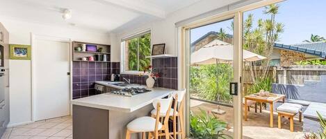 A modern kitchen with a central island, bar stools, and a sliding glass door leading to an outdoor patio with a table and chairs.
