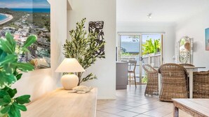 A modern living room with a view of the beach, a dining area with wicker furniture, and a large potted plant. - Sea Haven - Lennox Head (Lennox Head)