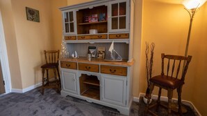 A room with a light blue wooden cabinet with multiple drawers and shelves, a small wooden chair, a floor lamp, and a carpeted floor. - 6 Guests-free Public Parking-5 Min to Beach (Porthcawl)