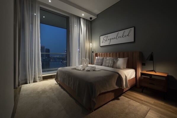 Une chambre moderne avec un grand lit, une vue sur la ville et une pancarte « #StayUnlocked » accrochée au mur.