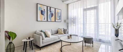 A modern living room with a sofa, a coffee table, and a large window with sheer curtains.