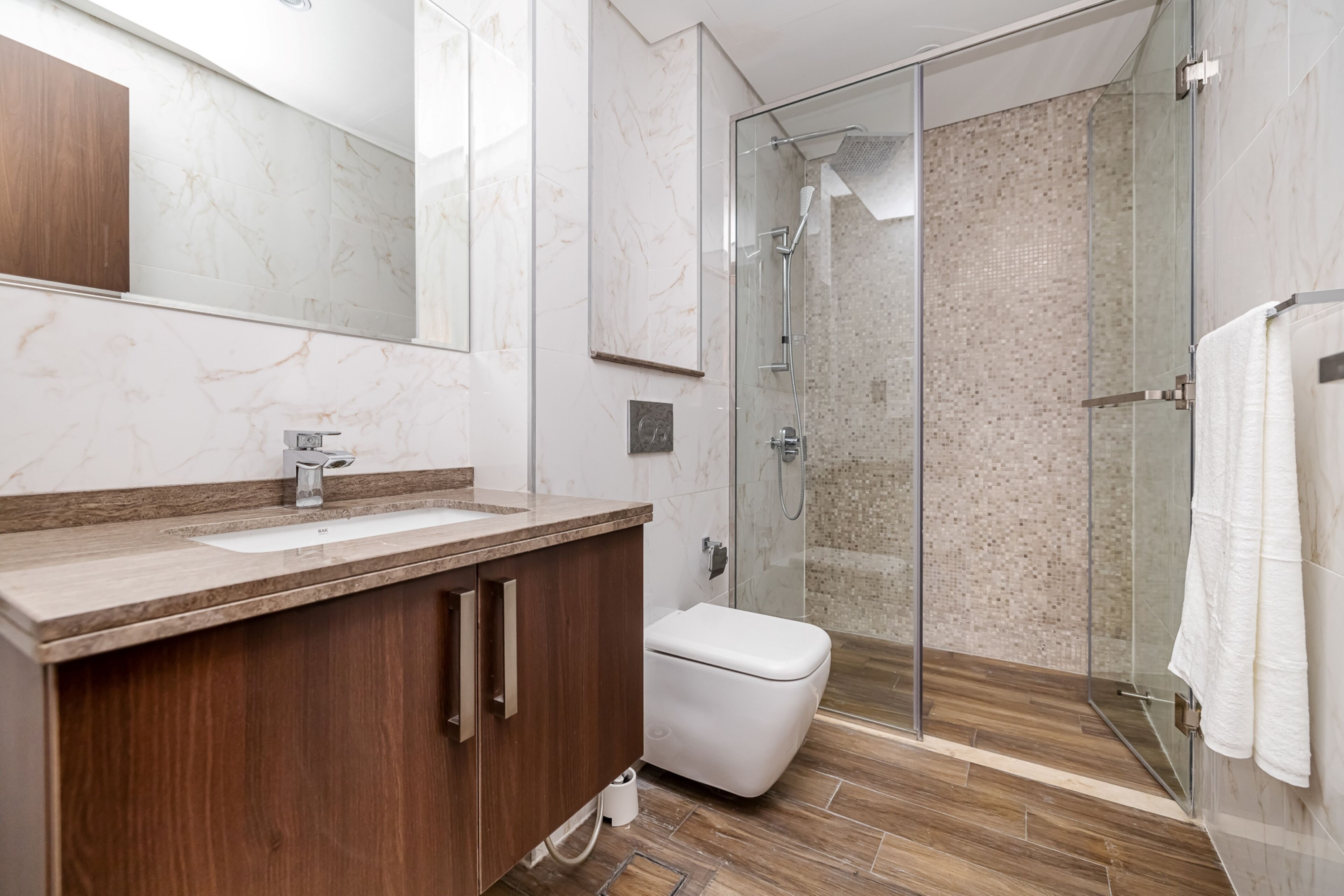 Ein modernes Badezimmer mit Marmorwaschtisch, einer Glasdusche und einer weißen Toilette.