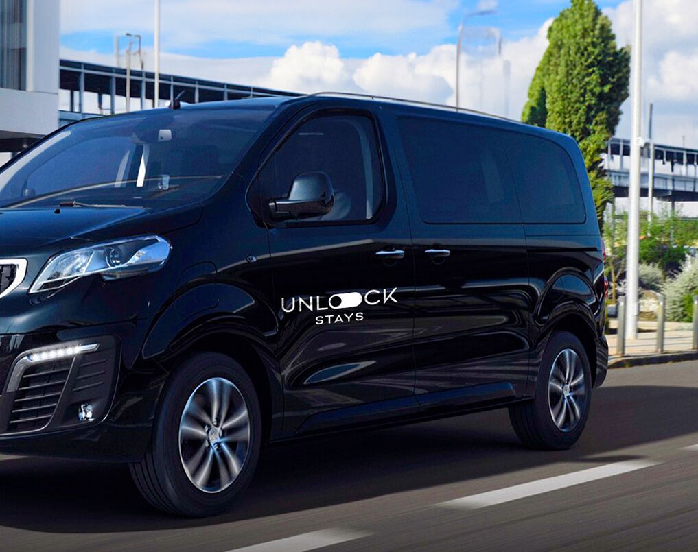 A black van with "UNLOCK STAYS" on the side, driving on a road.
