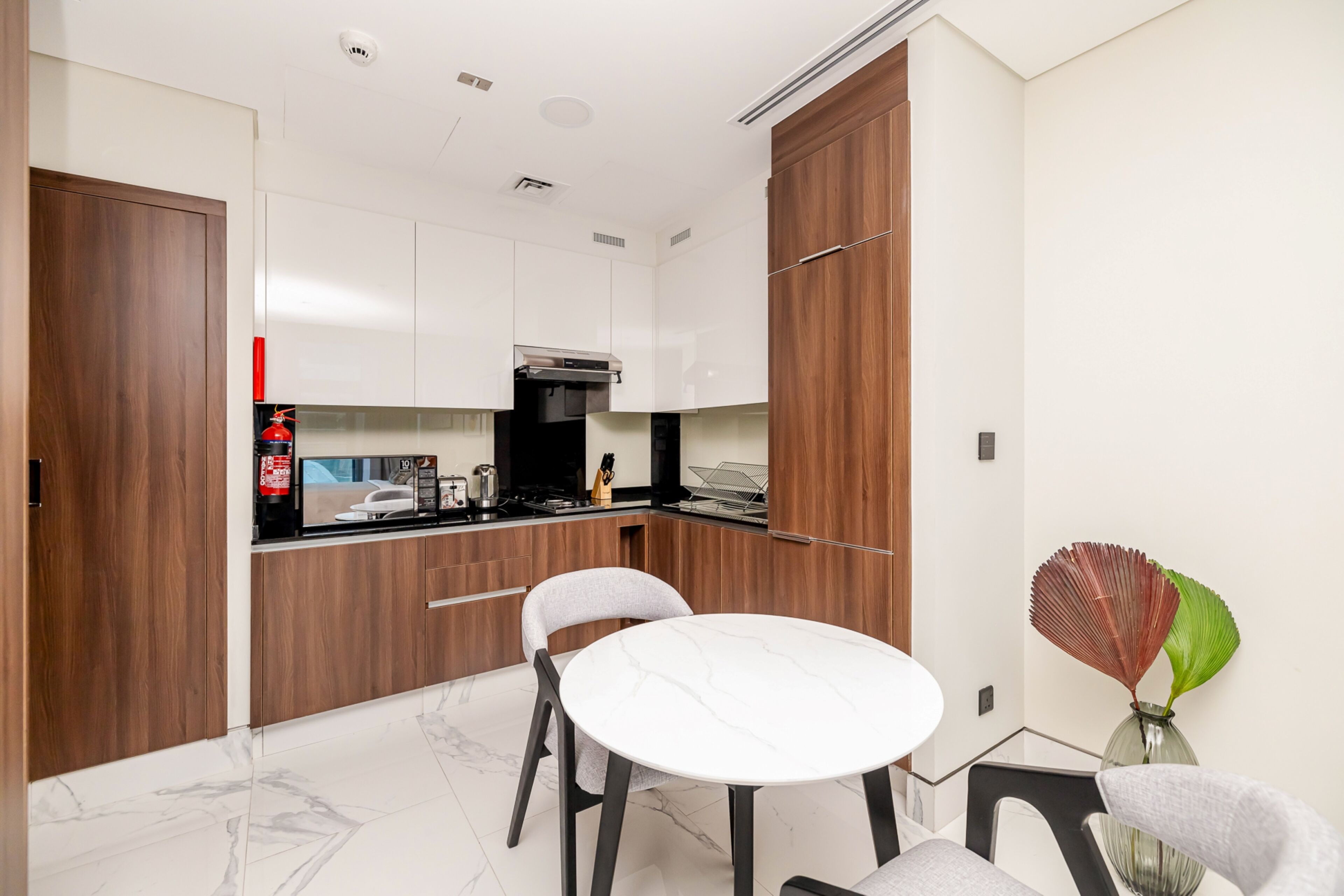 Una cocina moderna con armarios blancos, una pared de acento de madera, una mesa redonda para comer y un jarrón con hojas secas.
