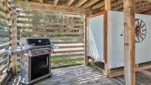 A covered outdoor area with a barbecue grill, wooden beams, and a white cabinet with a decorative wheel. - 5136- Bayside Breeze - Soundside KDH Retreat | Dog-Friendly (Kill Devil Hills)