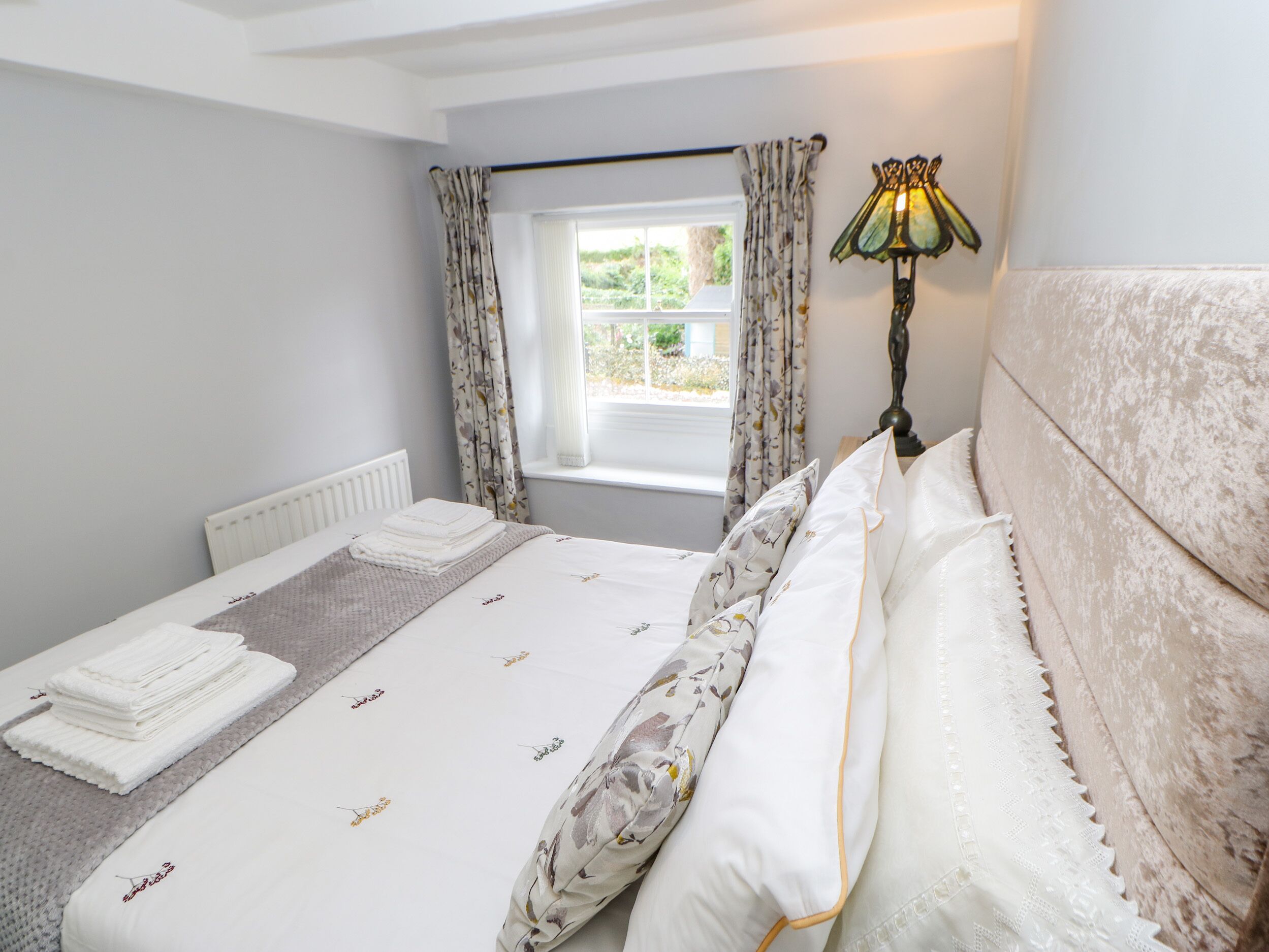 A neatly made bed with a floral duvet, a bedside lamp, and a window with curtains.