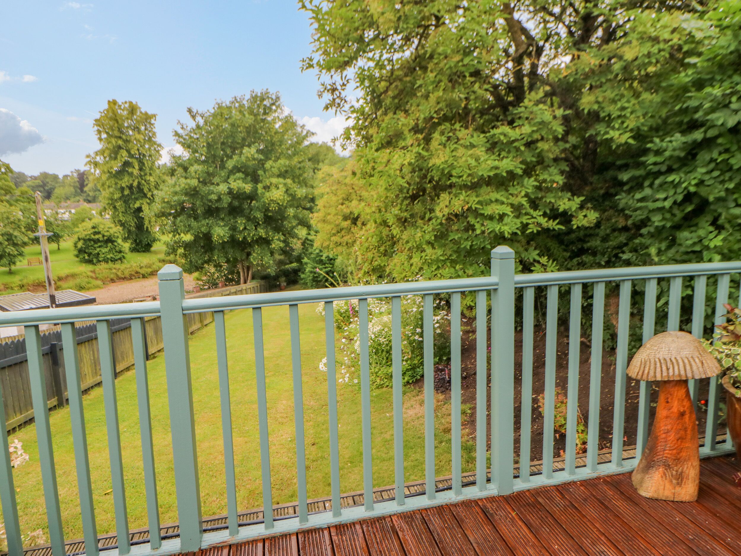 A wooden deck with a light blue railing, overlooking a grassy yard with trees and a wooden fence.