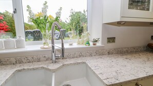 A kitchen with a double sink, a window with a view of greenery, and a countertop with kitchen items. - Eden Cottage (Appleby-in-Westmorland)