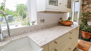 A kitchen with a white sink, marble countertop, and light-colored cabinets. - Eden Cottage (Appleby-in-Westmorland)