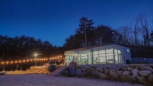A modern glass house with a stone wall foundation, surrounded by a stone pathway and string lights. - Yangyang In Memory Pension (Yangyang)