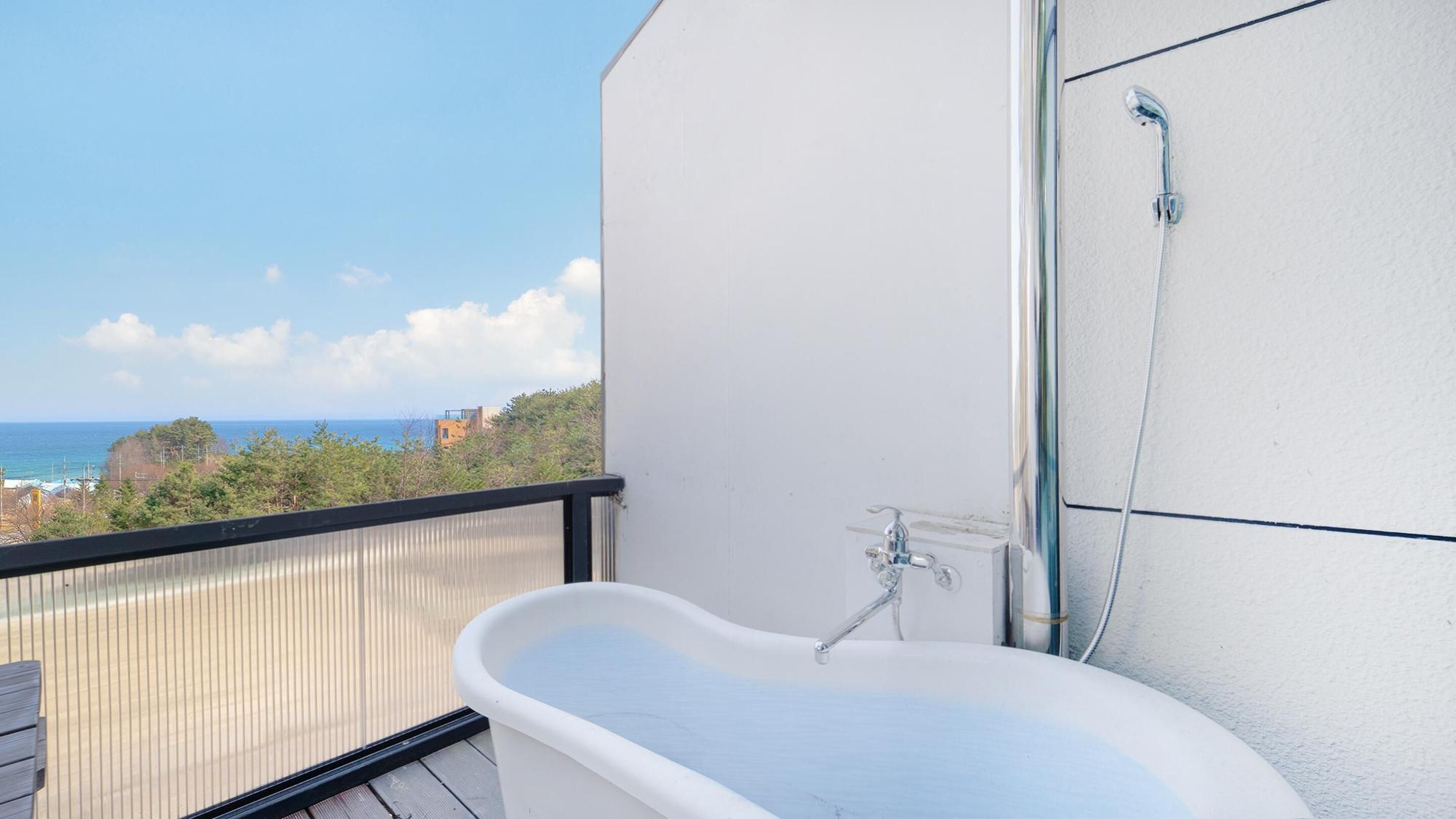 A balcony with a white bathtub, a shower, and a view of the ocean.