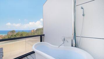 A balcony with a white bathtub, a shower, and a view of the ocean.